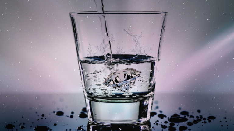 Close-up of a crystal glass filled with water and a diamond inside, with splashes around.