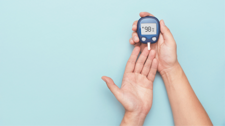 Hand holding a blue glucose meter showing 98 mg/dL against a light blue background]