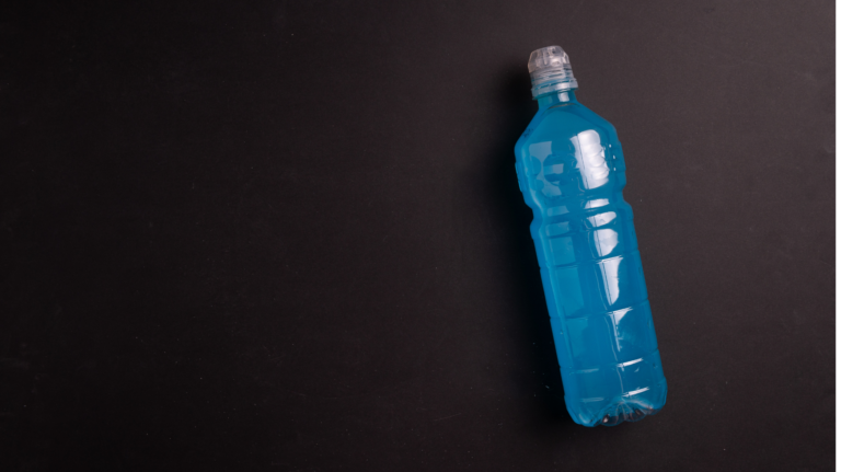 Blue plastic sports bottle lying diagonally on a dark surface, cap removed or open at the top edge visible on the right side.